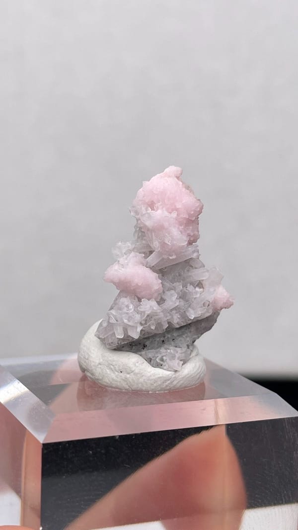 Pale pink rhodochrosite crust on grey quartz from Romania, on an acrylic stand, second angle