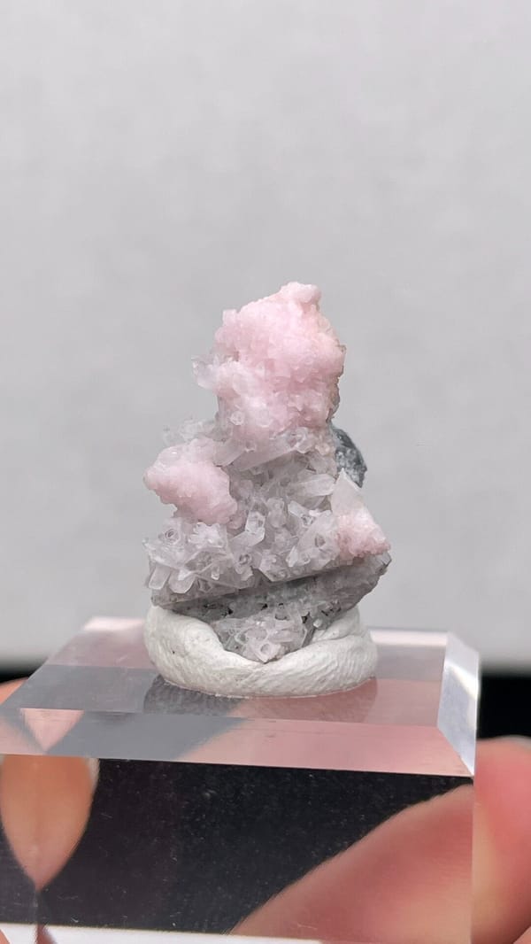 Pale pink rhodochrosite crust on grey quartz from Romania, on an acrylic stand, close-up of the crystal faces