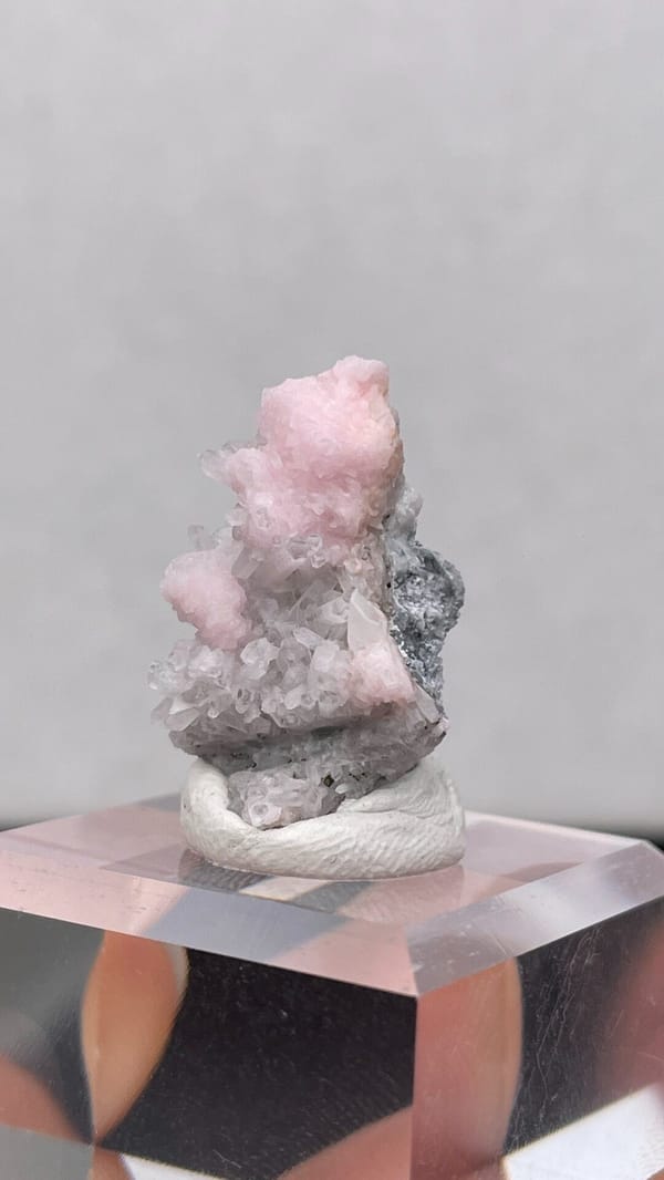 Pale pink rhodochrosite crust on grey quartz from Romania, on an acrylic stand, reverse side