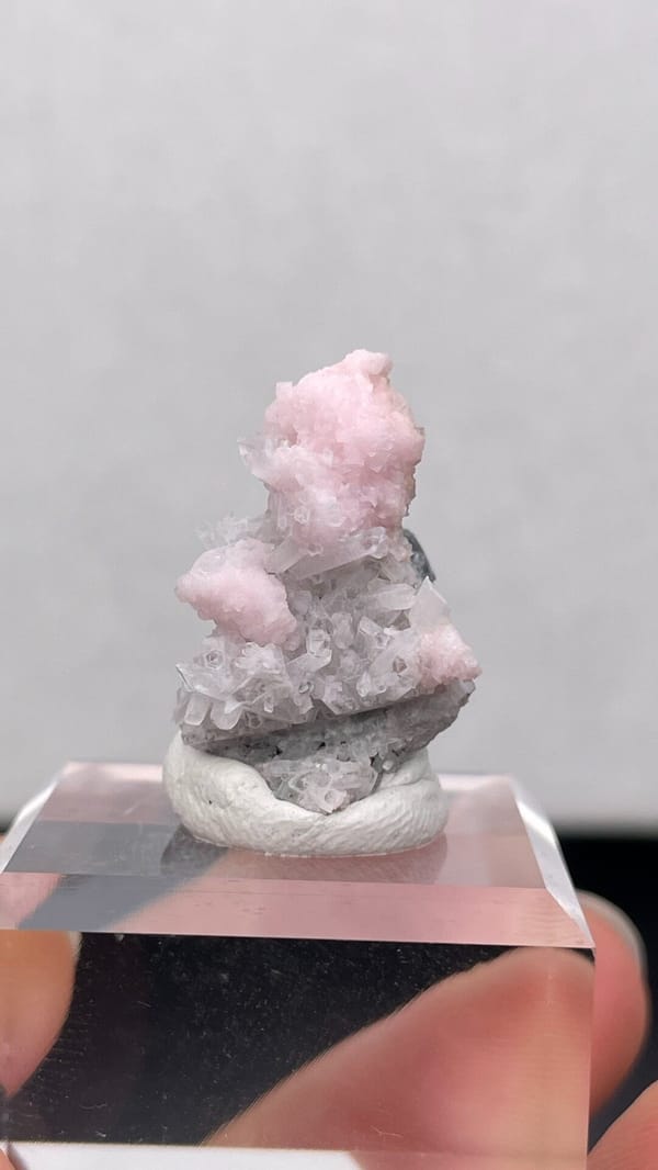 Pale pink rhodochrosite crust on grey quartz from Romania, on an acrylic stand, top view