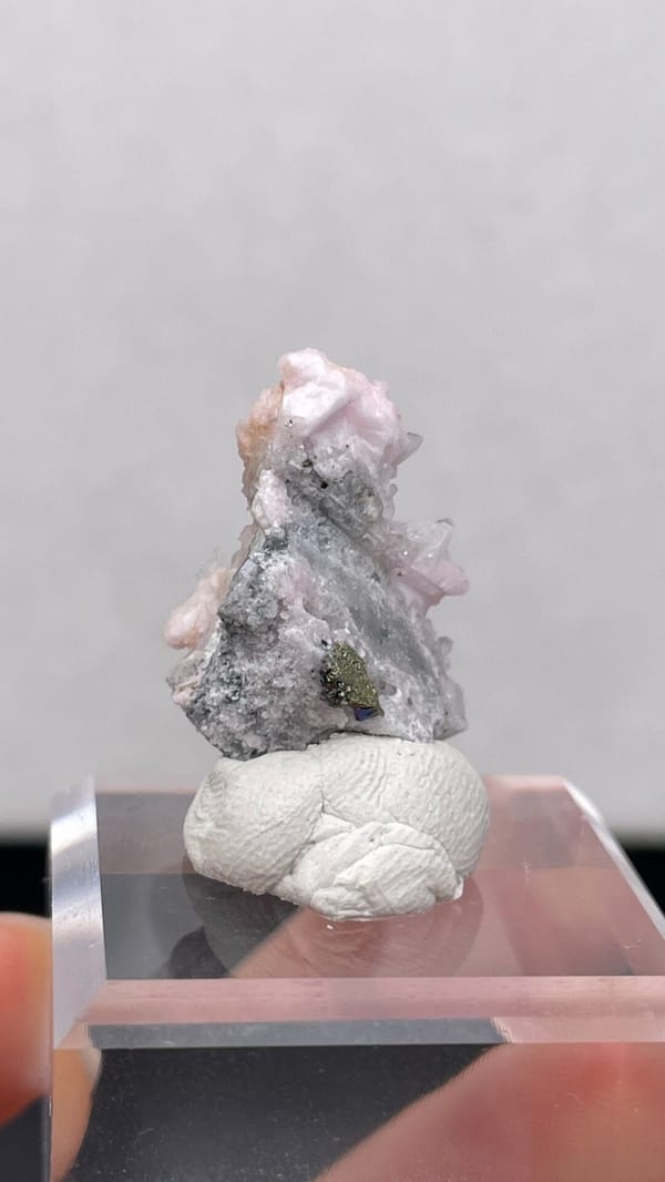 Pale pink rhodochrosite crust on grey quartz from Romania, on an acrylic stand, detail of the matrix contact