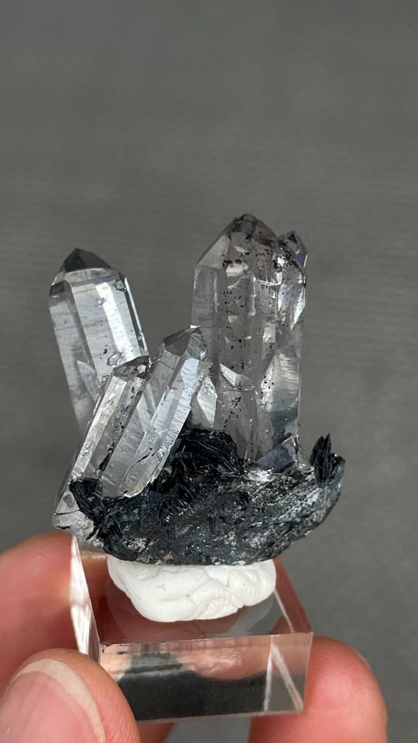 Clear quartz points on black specular hematite from Guangdong, China, on a stand