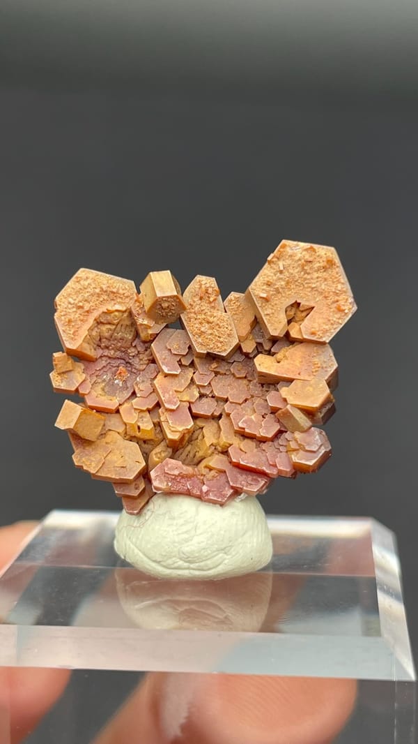 Stacked apricot-orange vanadinite plates from Morocco on an acrylic stand