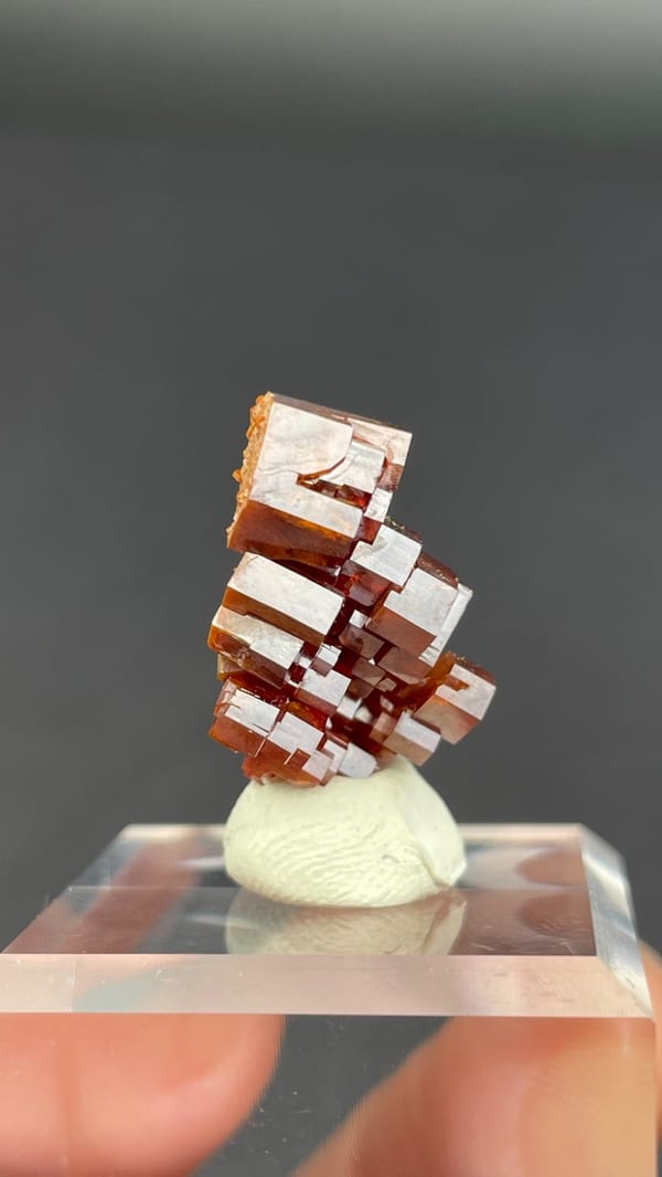 Stacked apricot-orange vanadinite plates from Morocco on an acrylic stand, second angle