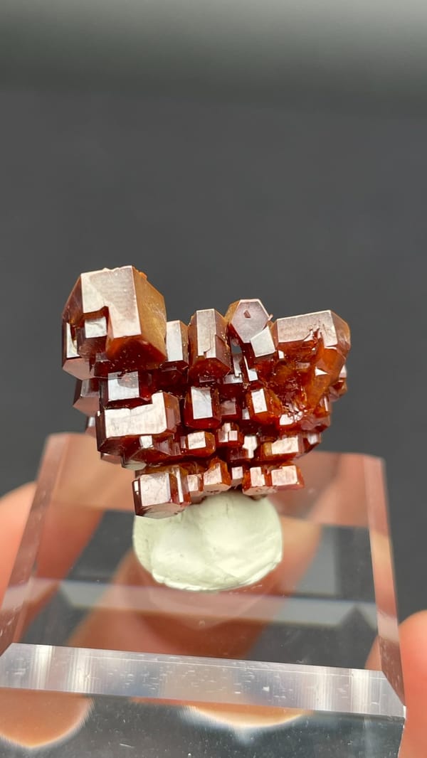 Stacked apricot-orange vanadinite plates from Morocco on an acrylic stand, reverse side