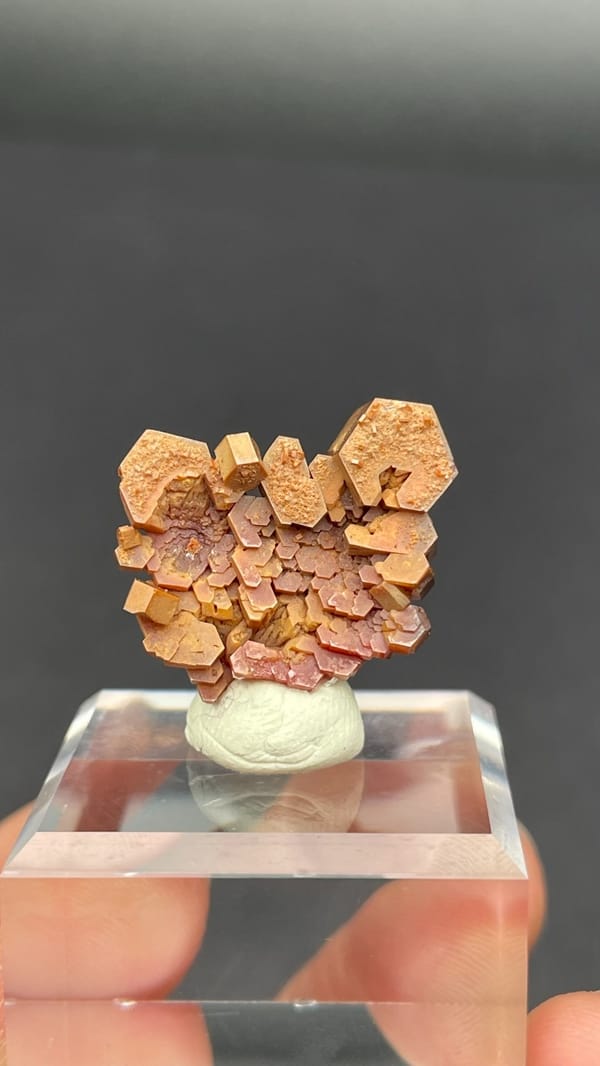 Stacked apricot-orange vanadinite plates from Morocco on an acrylic stand, detail of the matrix contact