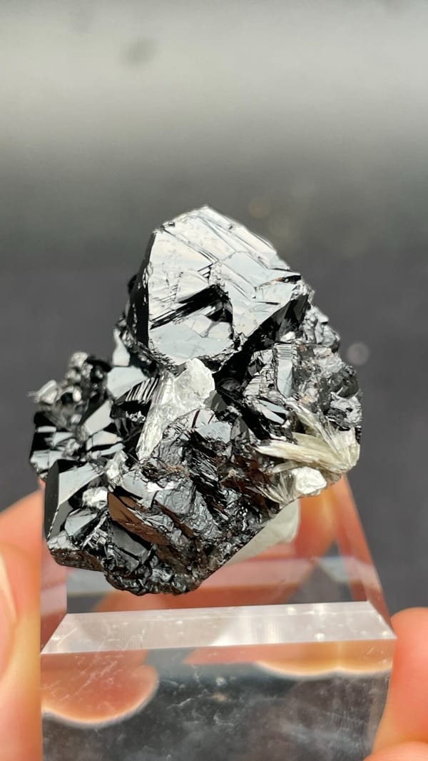 Black lustrous cassiterite with a clear quartz crystal from Xuebaoding, Sichuan, detail of the matrix contact