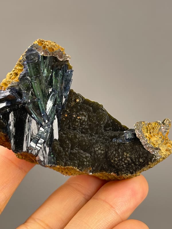 Vivianite from Brazil: dark green blades beside a rough yellow-brown edge.