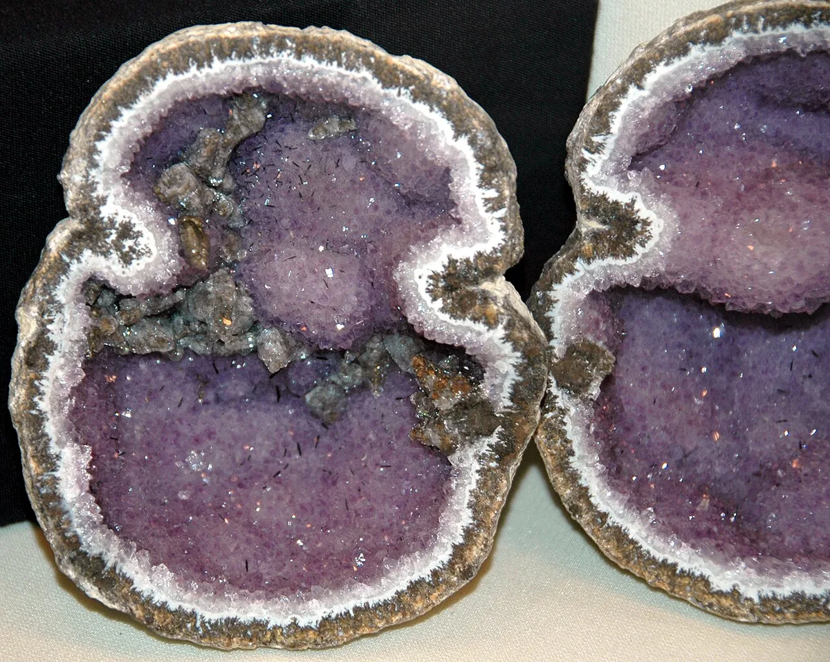 A geode cut in half, showing an agate rind and amethyst-lined cavity — minerals crystallizing inward into an open space.